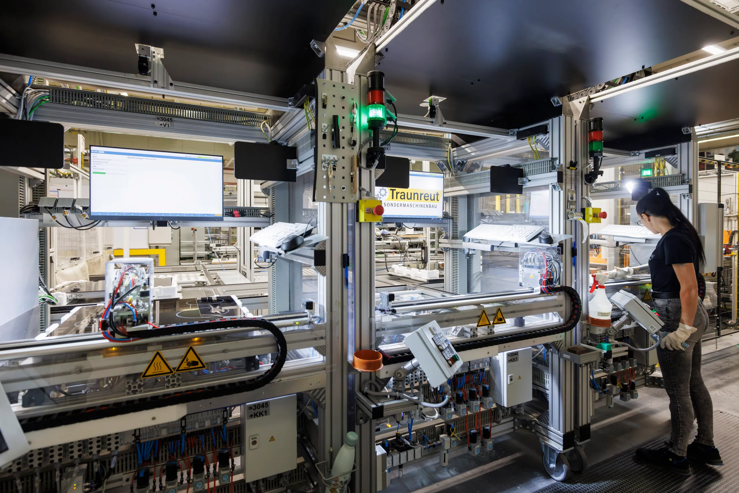 Eine Arbeitsstation mit mehreren Teststationen von Herdplatten ist abgebildet. Rechts im Bild steht eine Mitarbeiterin und kontrolliert die Teststation.