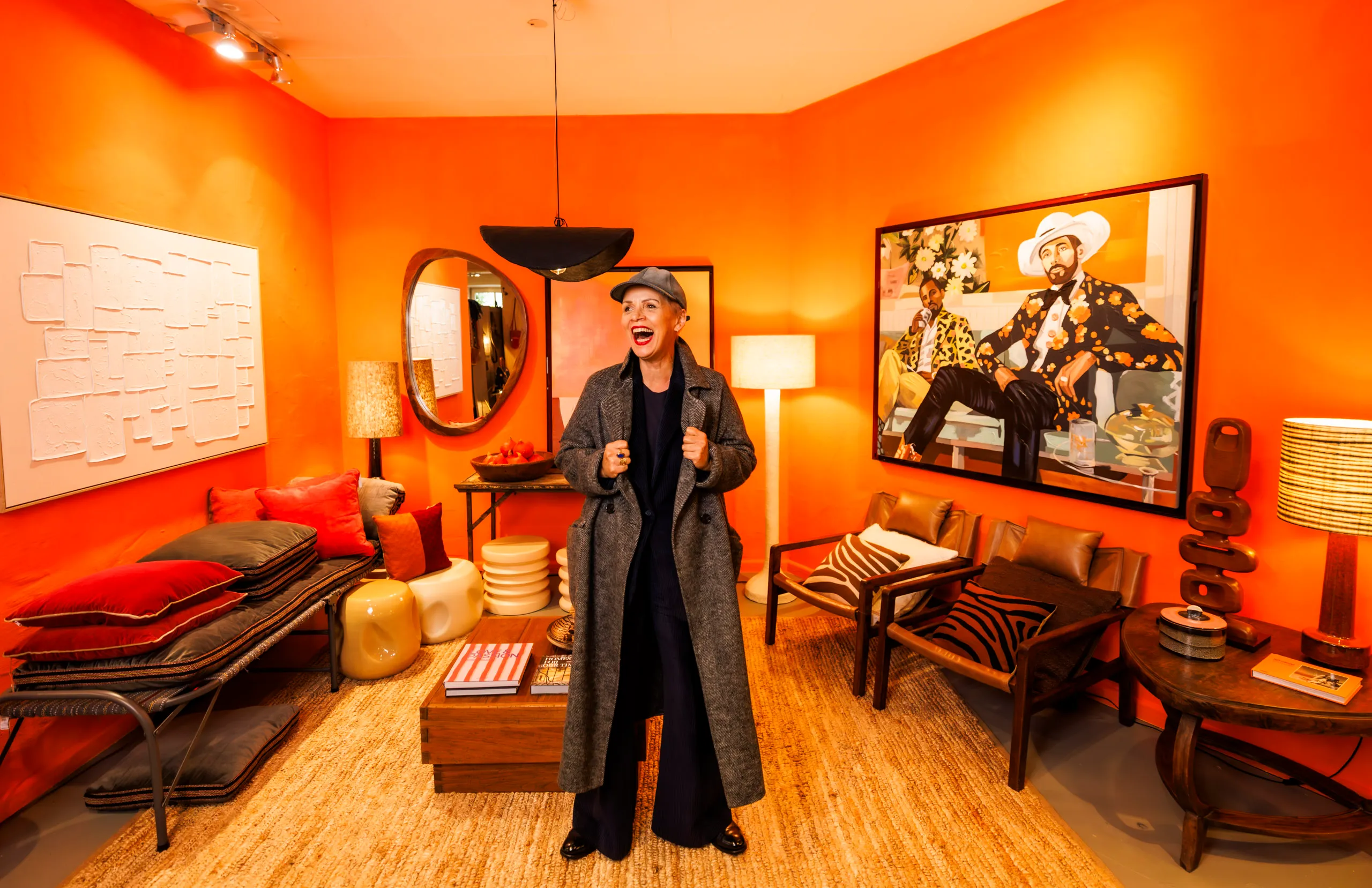 Eine Frau mit einem langen, grauen Mantel steht in einem orangefarbenen Wohnzimmer in einem Laden für Wohnaccessoires