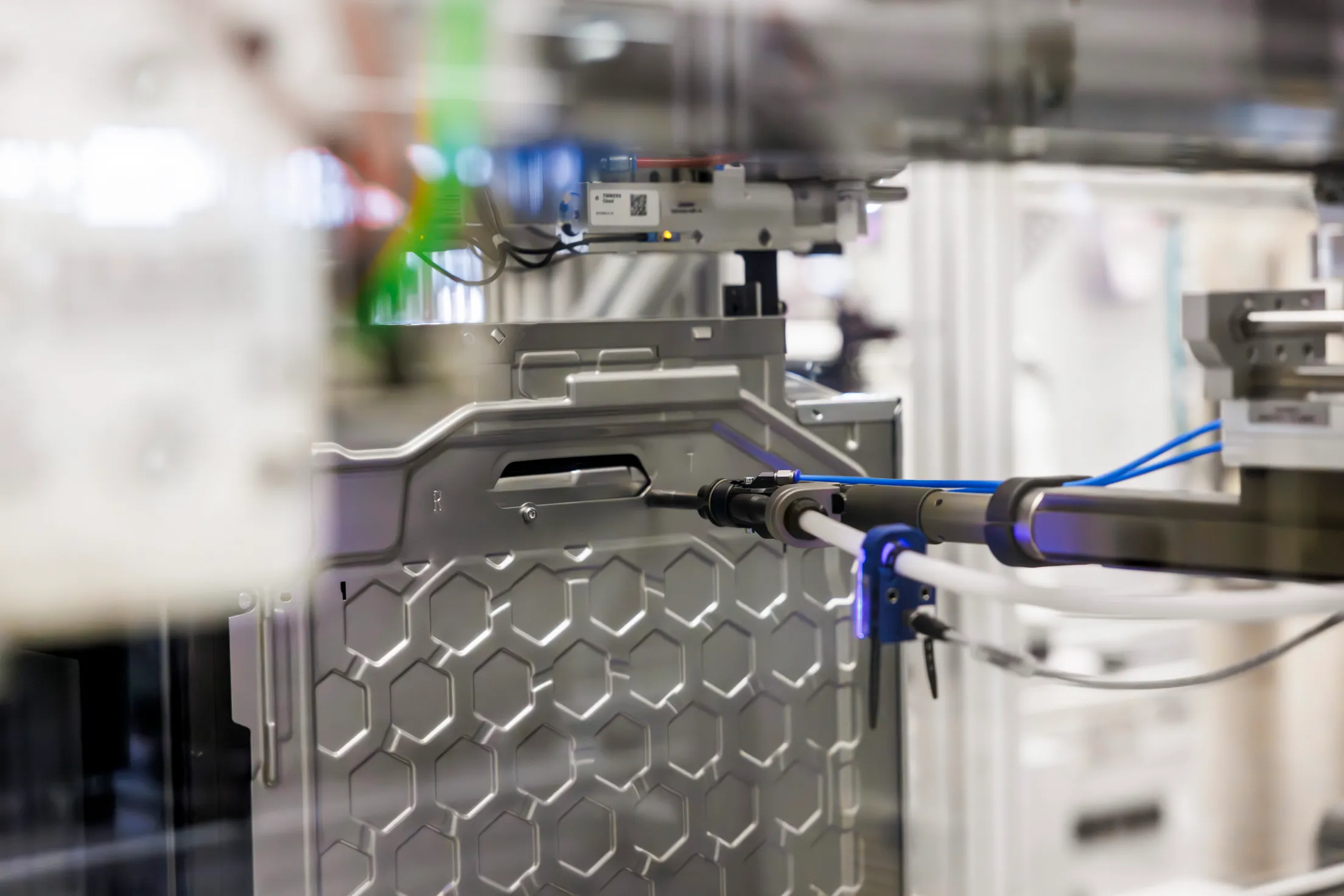 Detailaufnahmen von einer Backofen Rückseite. Ein Roboterarm schraubt automatisch Schrauben in die Rückwand. Es sind viele Unschärfen im Bild.